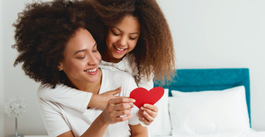 Mother and daughter enjoying on the bed, holding a heart